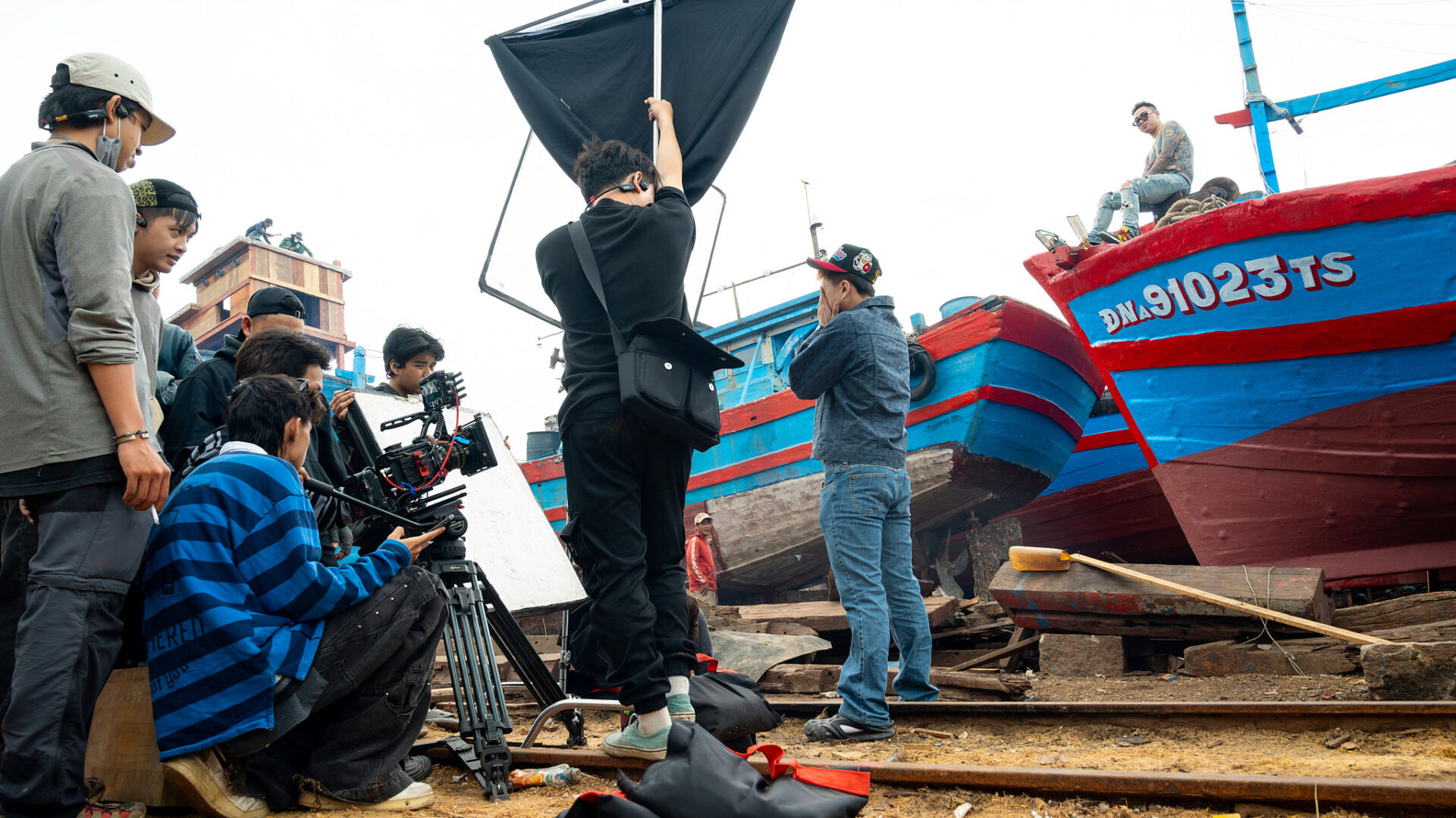 CINEFY crew filming beside a fishing boat in harsh daylight with one member shading the camera in Da Nang