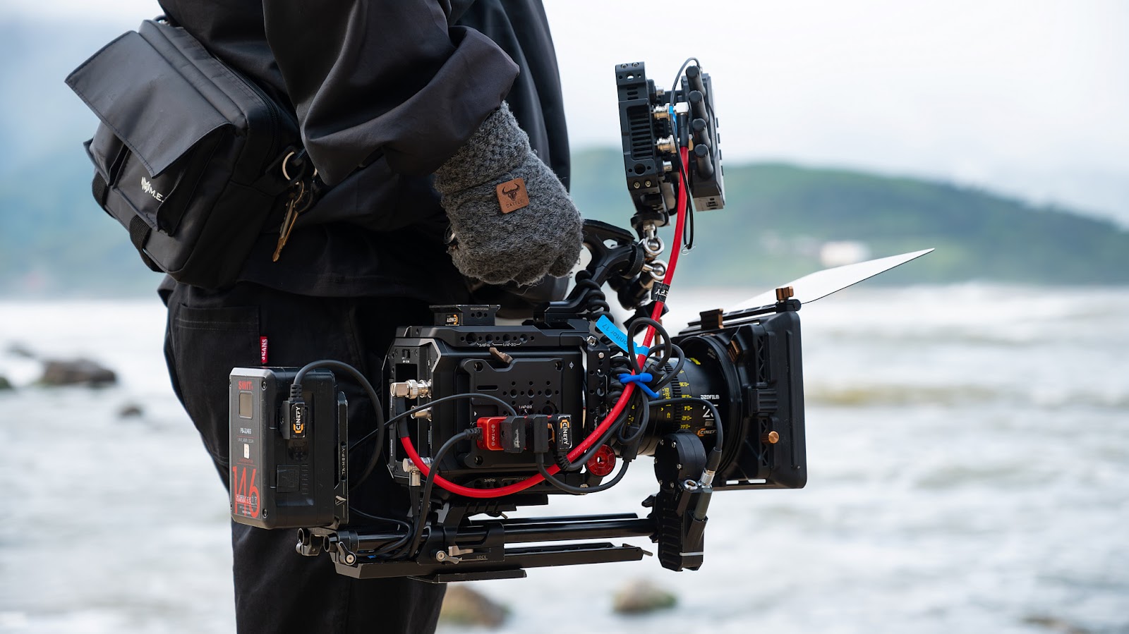A camera operator carries a compact cinema camera rig for an on-location video shoot on the Da Nang coast.