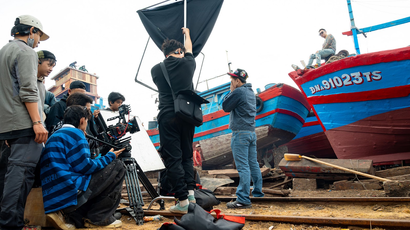 Production crew from a video production company in Da Nang filming on location beside a fishing boat in natural light.