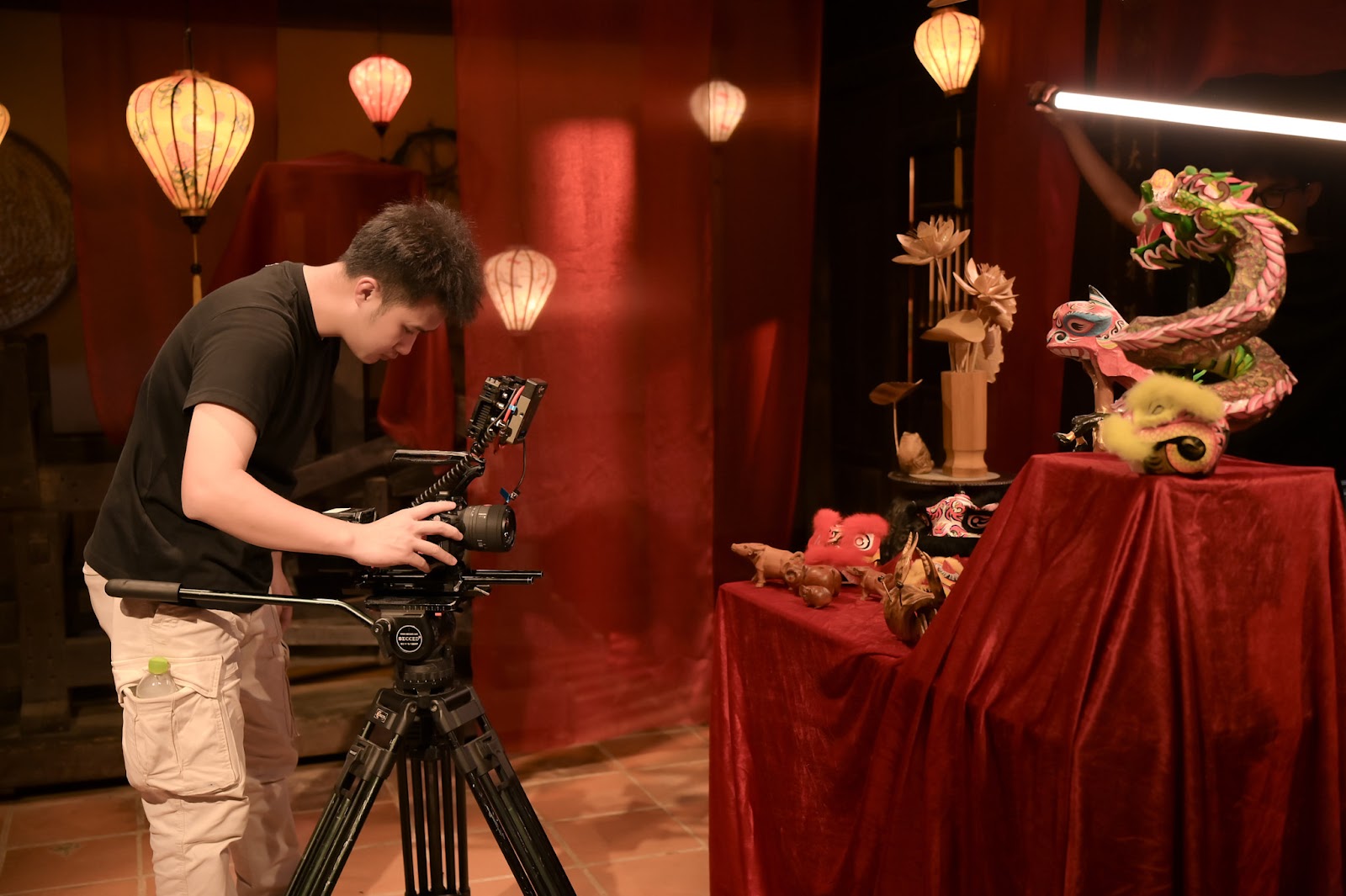 A director of photography behind a tripod mounted camera, framing an interior scene lit with warm practical lights