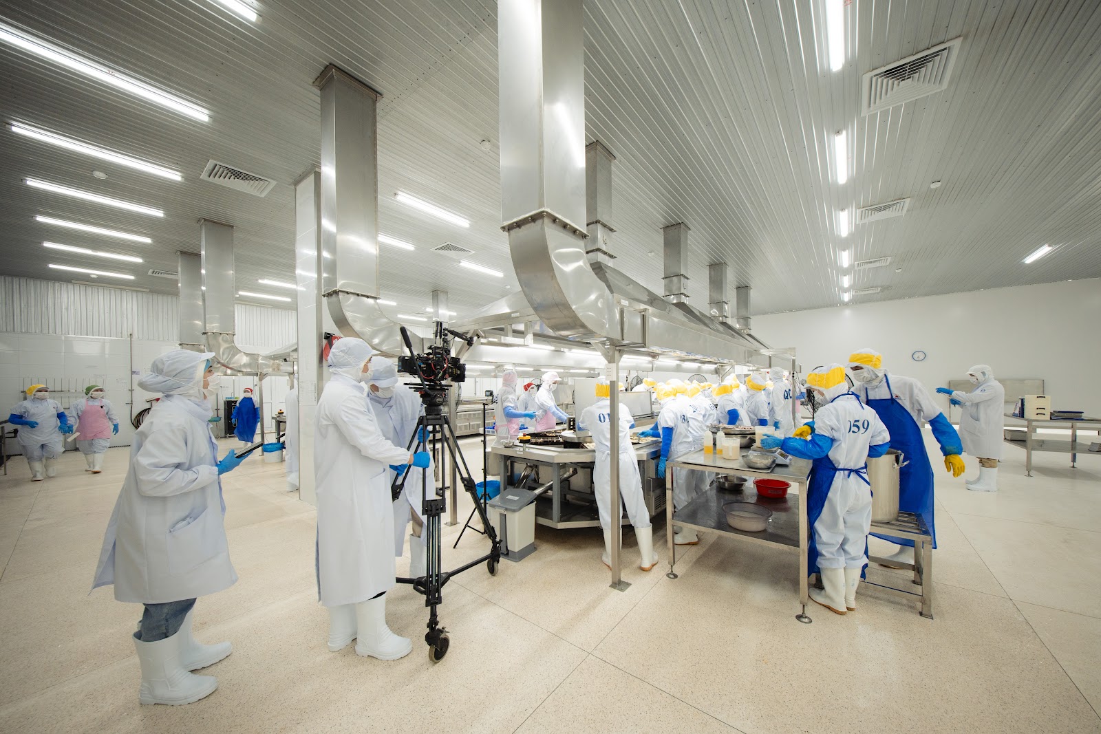 CINEFY crew member in a white coat, hair cover and boots like the workers, standing next to a camera on a tripod at a processing table
